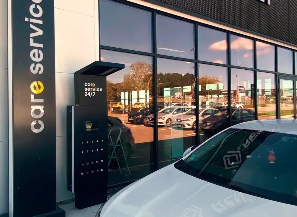 Borne à casiers connectés contre la façade vitrée d’une concession automobile